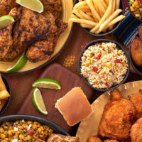 A closeup spread of Pollo Campero's menu items, including grilled chicken, french fries, street corn salad, rice, roasted potatoes, chicken salad, and fried chicken.