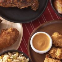 A large, square image of Pollo Campero's chicken, including chicken wings, fried chicken, rice and dipping sauce.