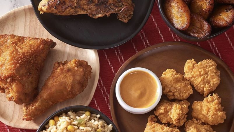 A large, square image of Pollo Campero's chicken, including chicken wings, fried chicken, rice and dipping sauce.